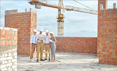 Important information. Three men in white shirt and protective helmet and woman in business suit with drawings looking into laptop standing in building under construction